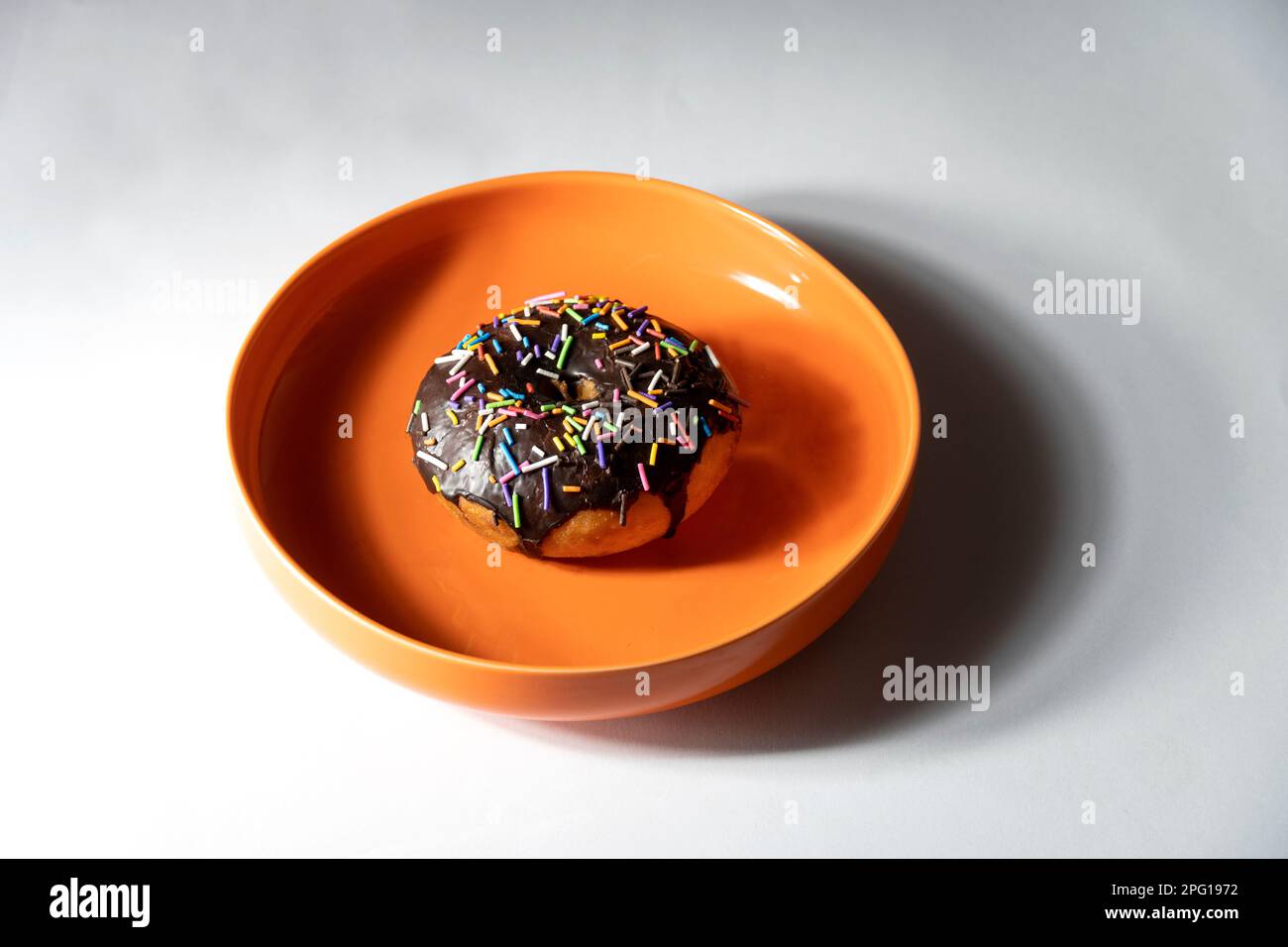 Ciambella colorata in piatto arancione su sfondo bianco. Vista dall'alto Foto Stock