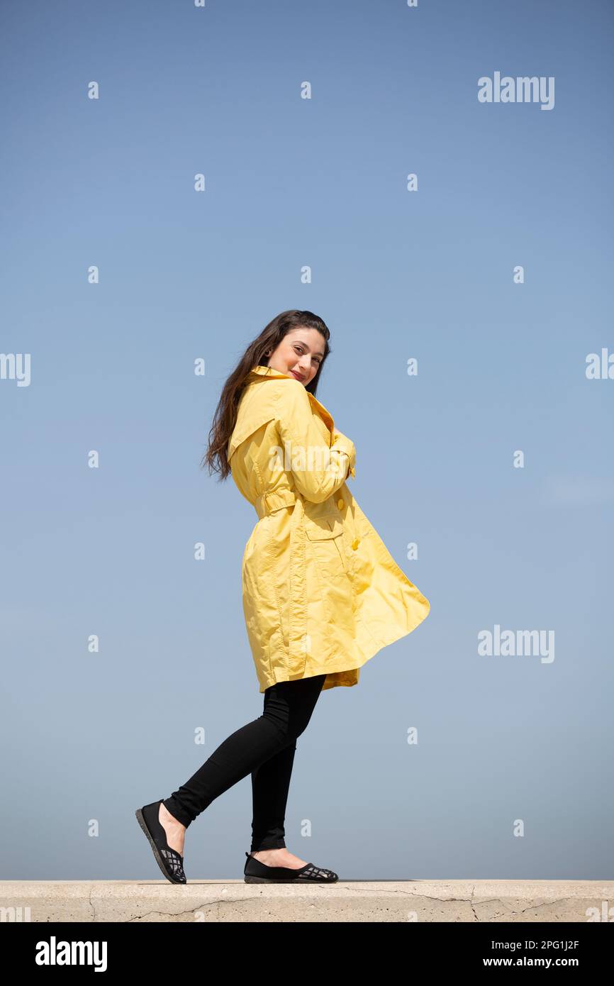 Bella donna in cappotto giallo guardando la fotocamera sorridente all'aperto Foto Stock
