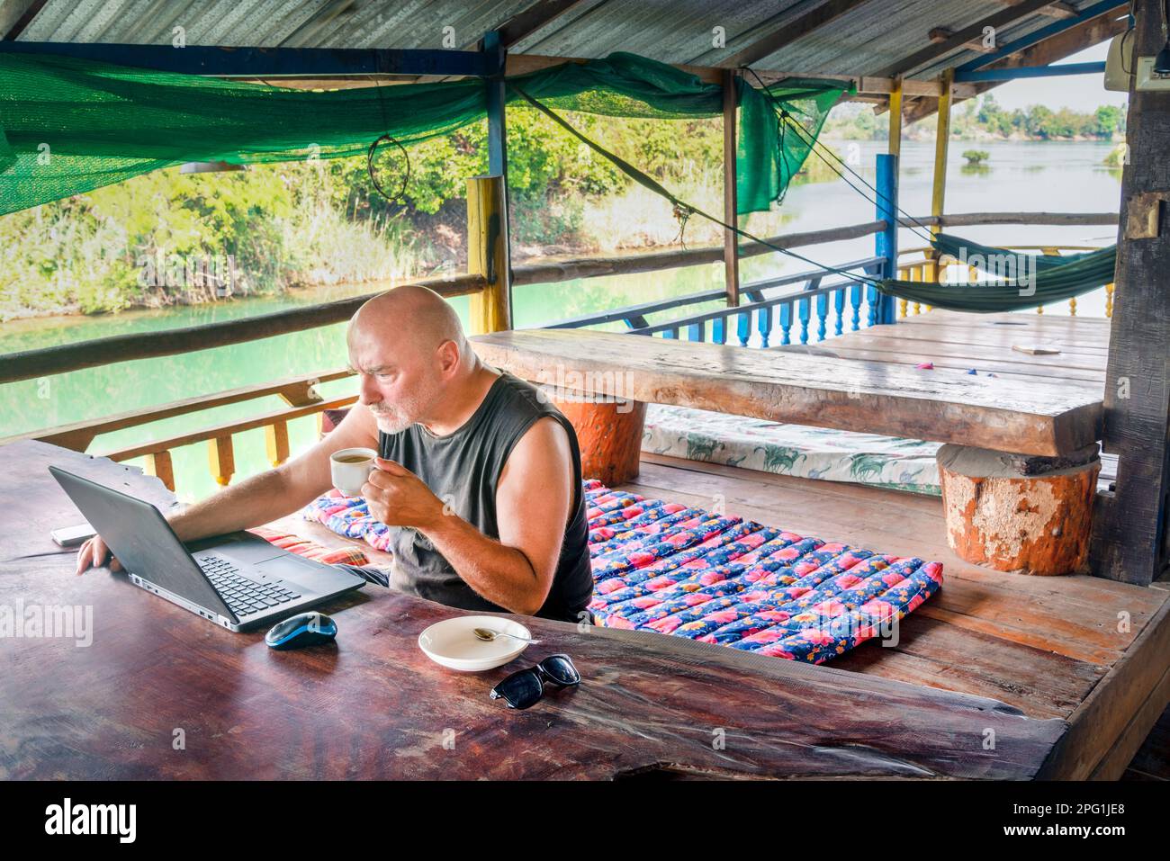 Lavorando a distanza sul suo computer a si Phan Don, un uomo che viaggia per il mondo, si siede su un balcone in una pensione rurale, che si affaccia sul fiume Mekong, con un Foto Stock