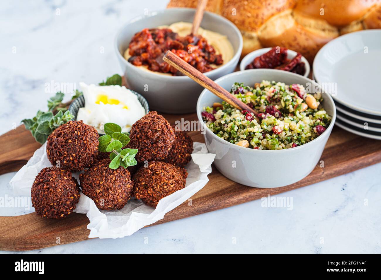 Tavolo tradizionale Shabbat: pane challah, falafel, insalata di quinoa, hummus su un asse di legno. Concetto di cibo israeliano. Foto Stock