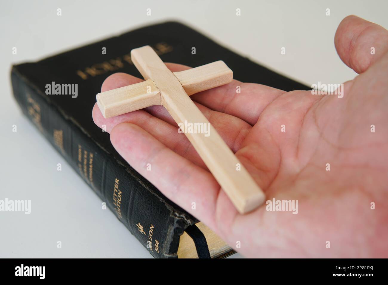 Cristiano cattolico uomo che tiene una croce. Vecchia Bibbia Santa sul tavolo. Foto Stock