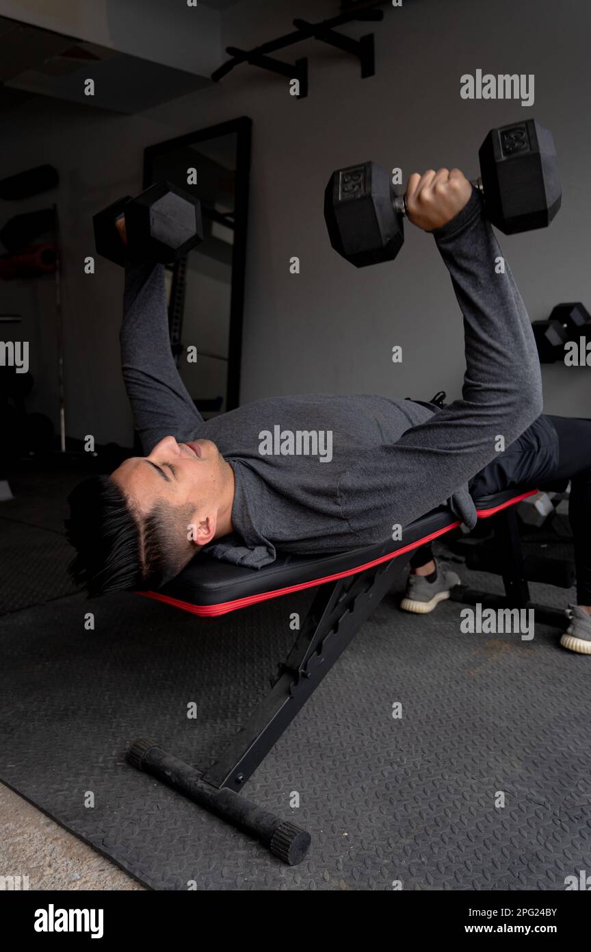 Panca giovane uomo che preme i dumbbells a in palestra del garage domestico Foto Stock