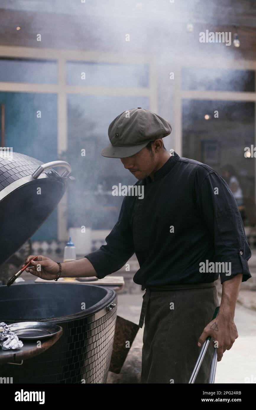 L'uomo asiatico in uniforme cucina sulla griglia all'aperto. Personale di cucina, Foto Stock