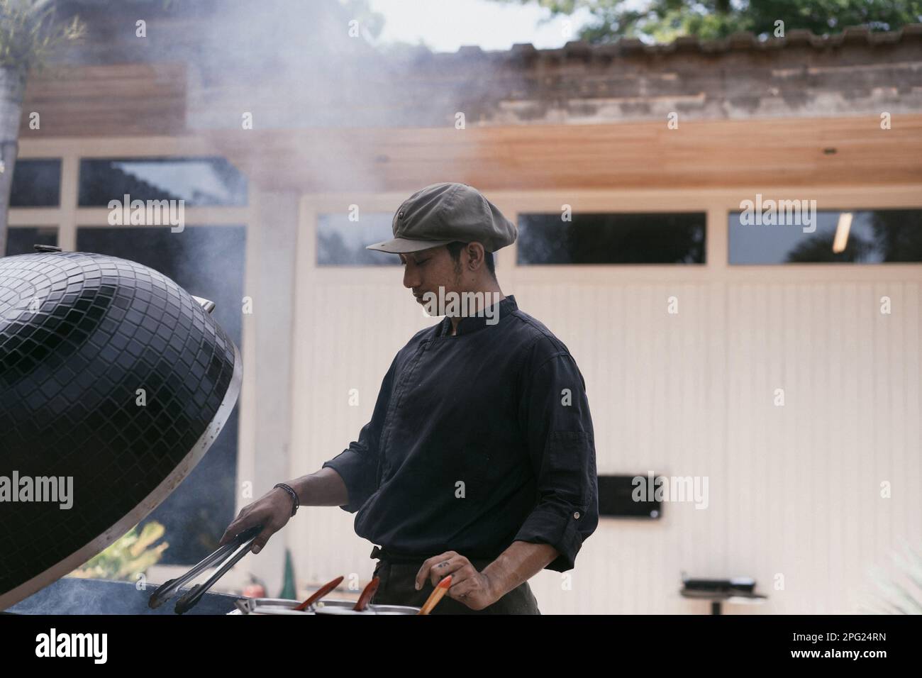 L'uomo asiatico in uniforme cucina sulla griglia all'aperto. Personale di cucina, Foto Stock