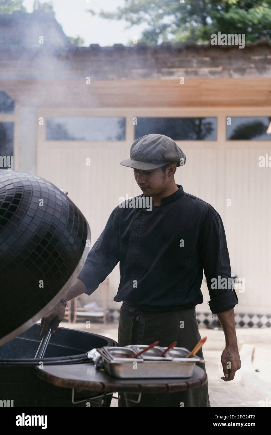 L'uomo asiatico in uniforme cucina sulla griglia all'aperto. Personale di cucina, Foto Stock