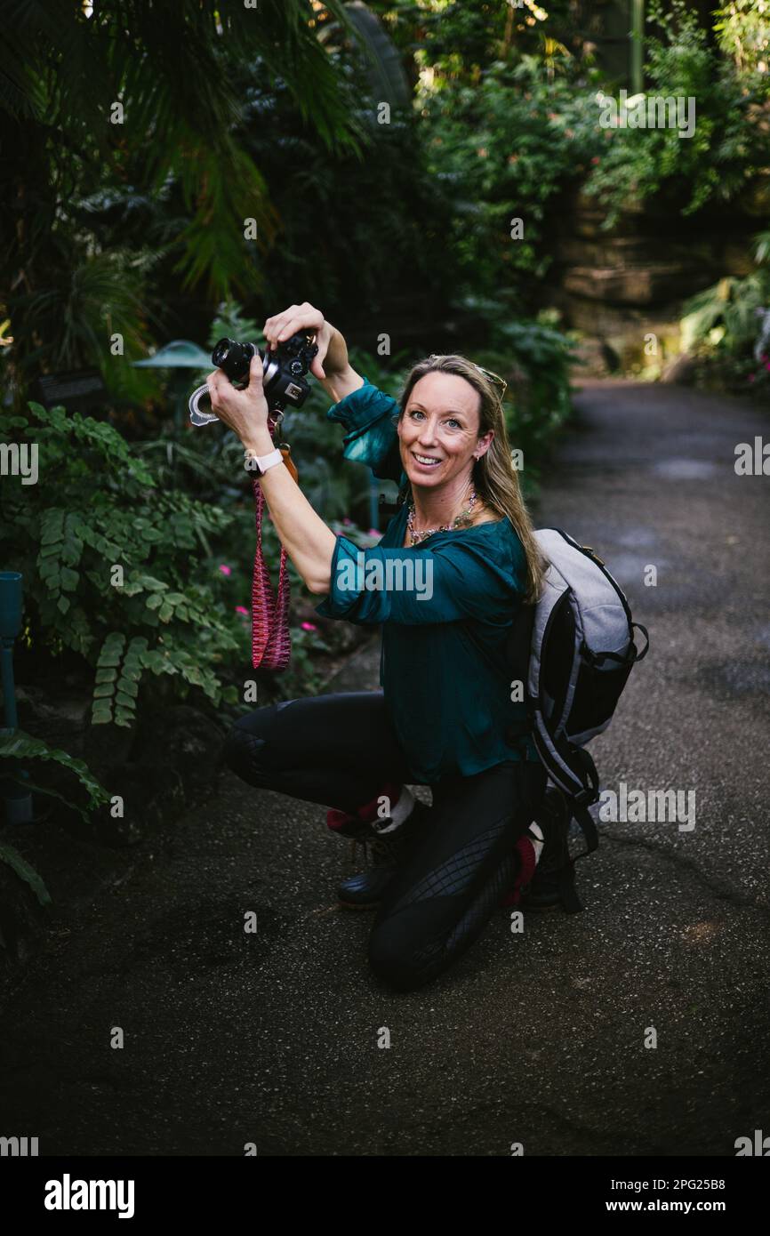 Donna con macchina fotografica e zaino in verde lussureggiante foresta fotografando Foto Stock