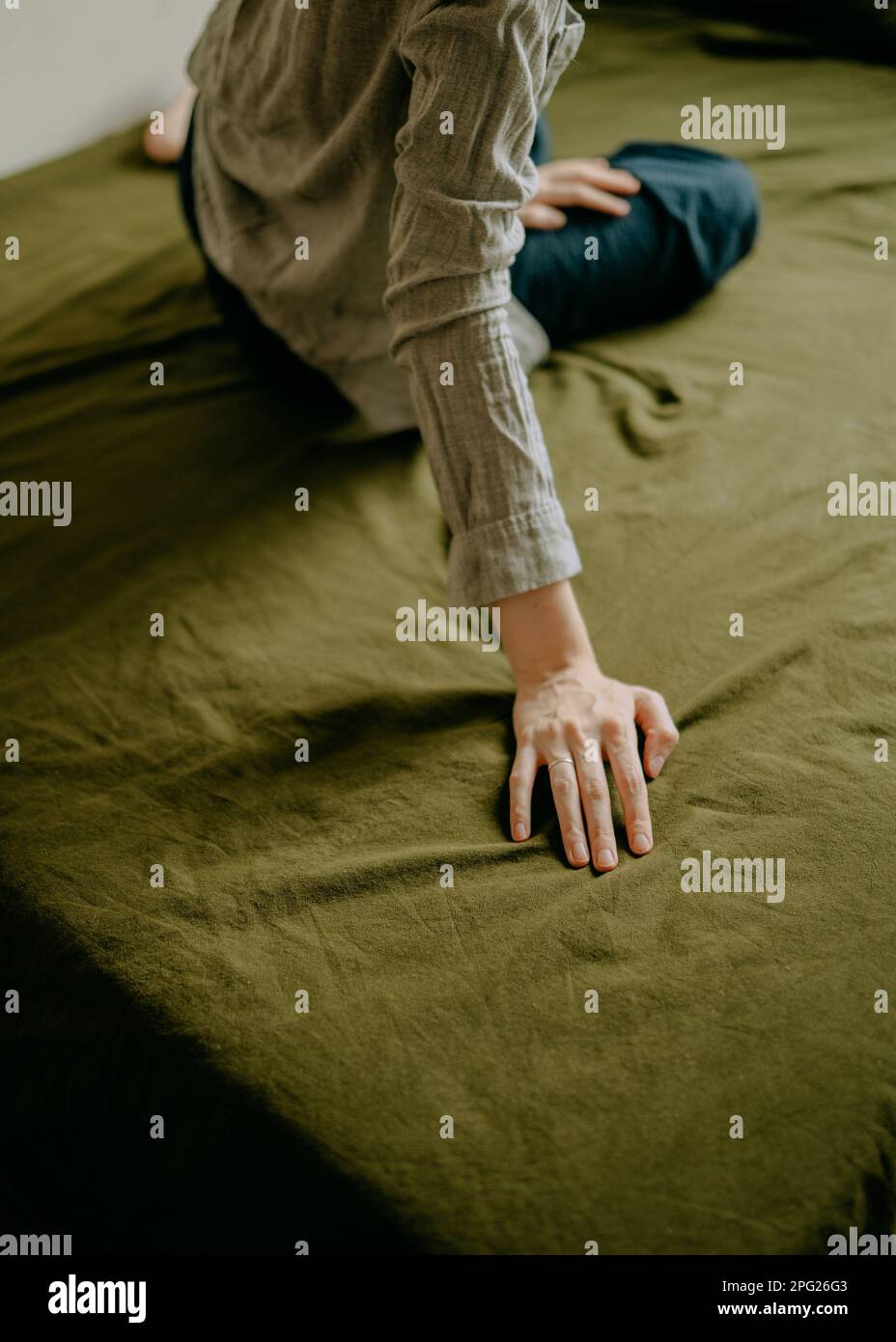 Mano di una donna seduta su un letto con lenzuola verdi Foto Stock