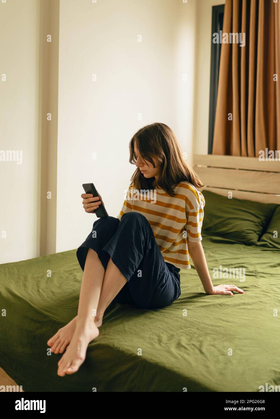Giovane donna che guarda il telefono mentre si siede su un letto Foto Stock