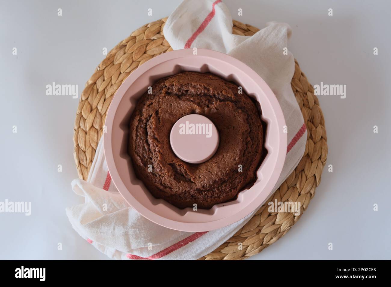 Torta al forno in uno stampo, c'è una torta di cacao al forno in uno stampo di silicone rotondo rosa su un panno da cucina bianco e un placemat sul tavolo da cucina. Foto Stock