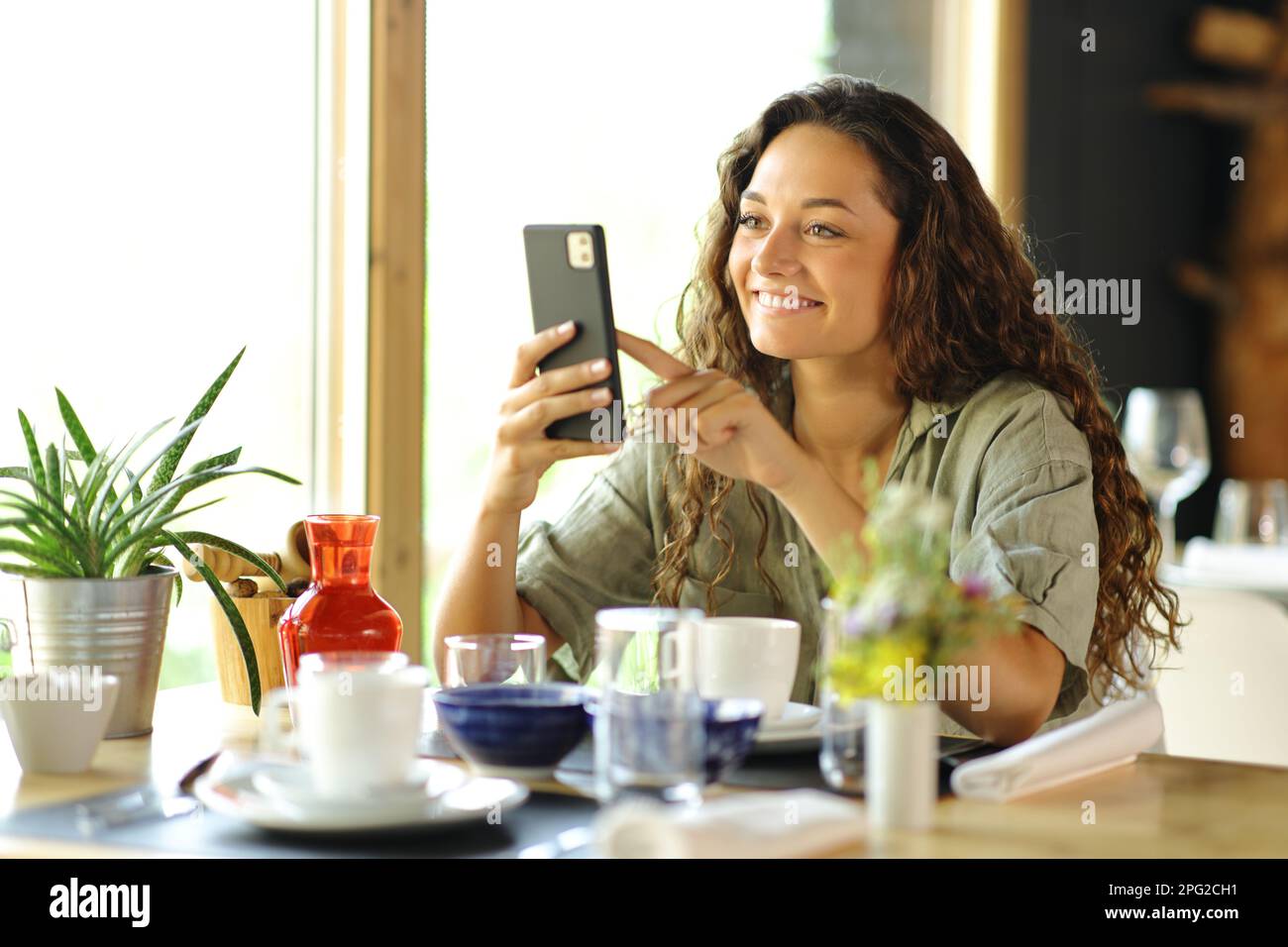 Una donna felice controlla lo smartphone a colazione in un ristorante Foto Stock