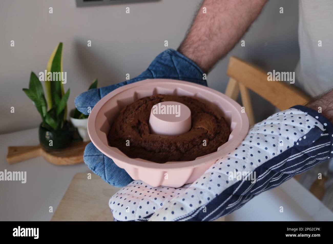 Torta al forno in uno stampo di silicone, l'uomo mette una torta di cacao in uno stampo di silicone rotondo rosa su un tagliere di legno in cucina. Cacao torta di concetto foto. Foto Stock