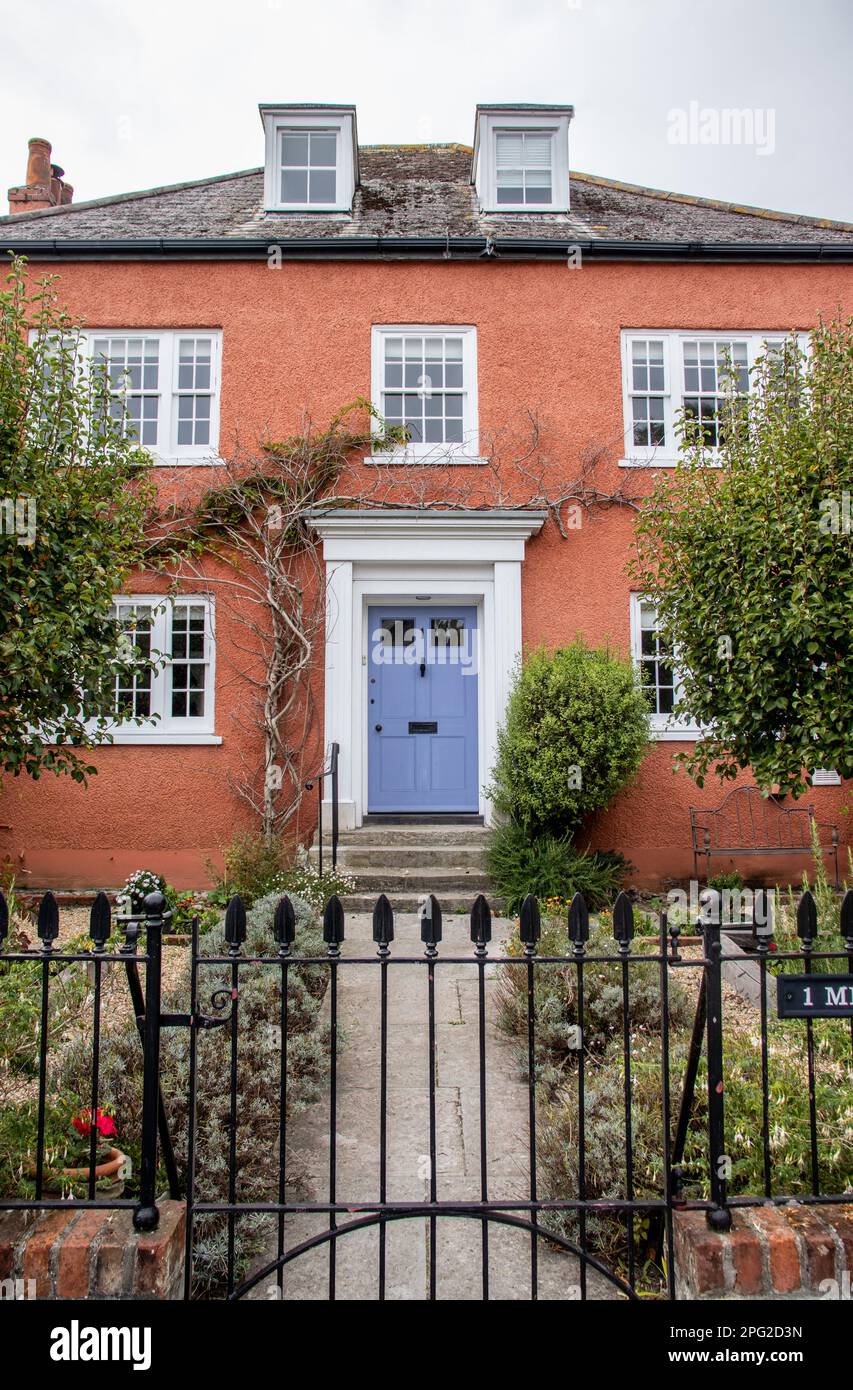 Una tipica casa Dorset in Inghilterra. Con pareti esterne dipinte in terracotta, una porta lilla e un giardino formale e un cancello e sentiero frontale. Foto Stock