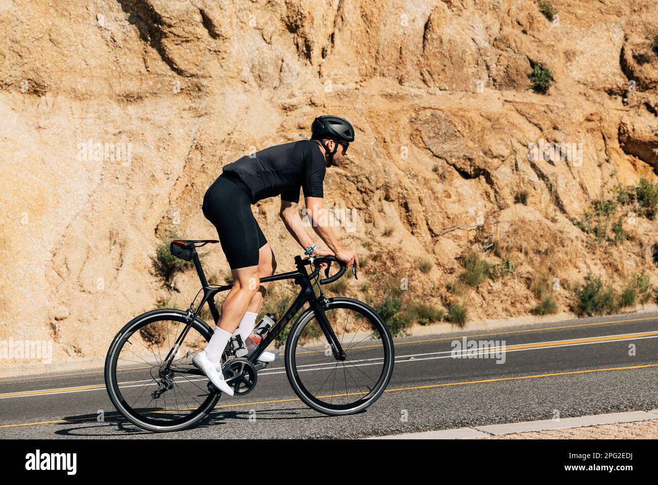 Ciclista in abbigliamento sportivo nero che fa un intenso allenamento all'aperto. Vista laterale di un triatleta in bicicletta. Foto Stock
