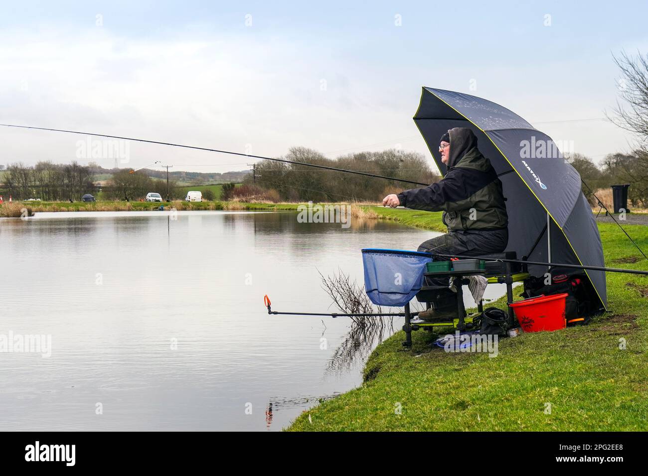 Pescatore seduto al bordo di un lago di pesca vicino a Tarbolton, Ayrshire, Scozia, Regno Unito Foto Stock