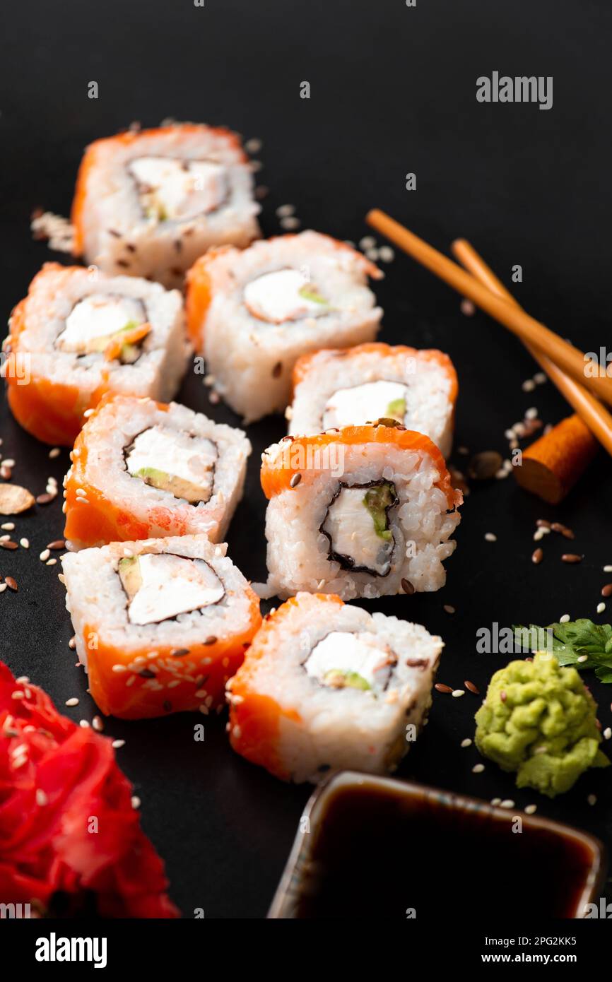 La gamma di diversi tipi di sushi e panini giapponesi. Su sfondo rustico scuro. Rotola su sfondo scuro. Set di pesce con bacchette. Foto Stock