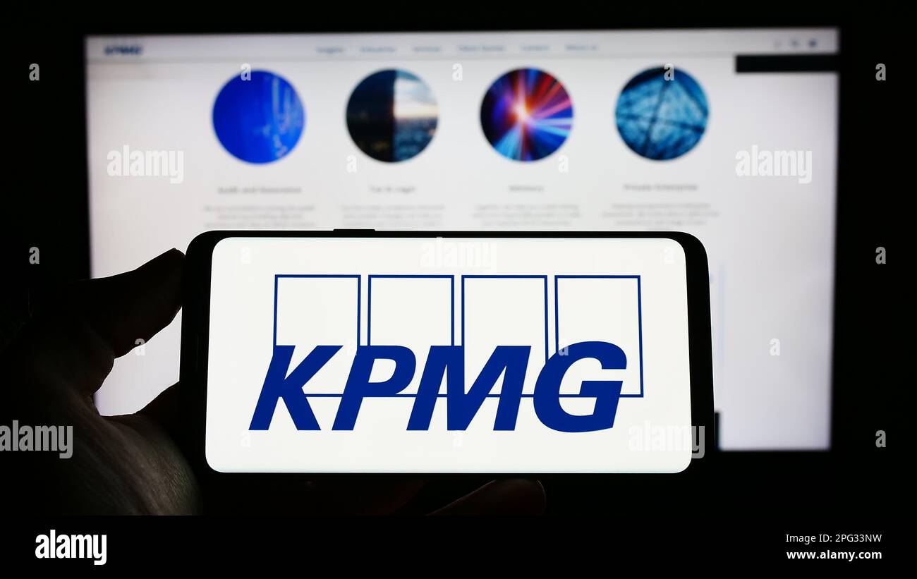 Persona che tiene il cellulare con il logo della società di servizi professionali KPMG sullo schermo di fronte al sito web aziendale. Messa a fuoco sul display del telefono. Foto Stock
