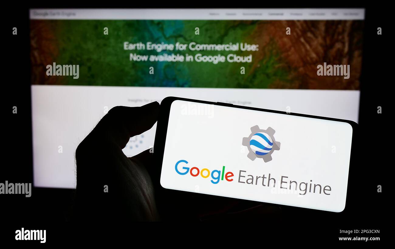 Persona che tiene il cellulare con il logo del prodotto software Google Earth Engine sullo schermo di fronte alla pagina web aziendale. Messa a fuoco sul display del telefono. Foto Stock