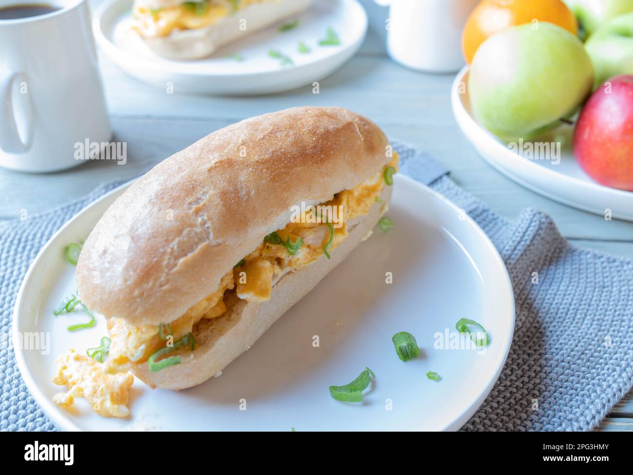 Sandwich per la colazione con uova strapazzate e tazza di caffè al mattino su un tavolo da cucina a casa Foto Stock