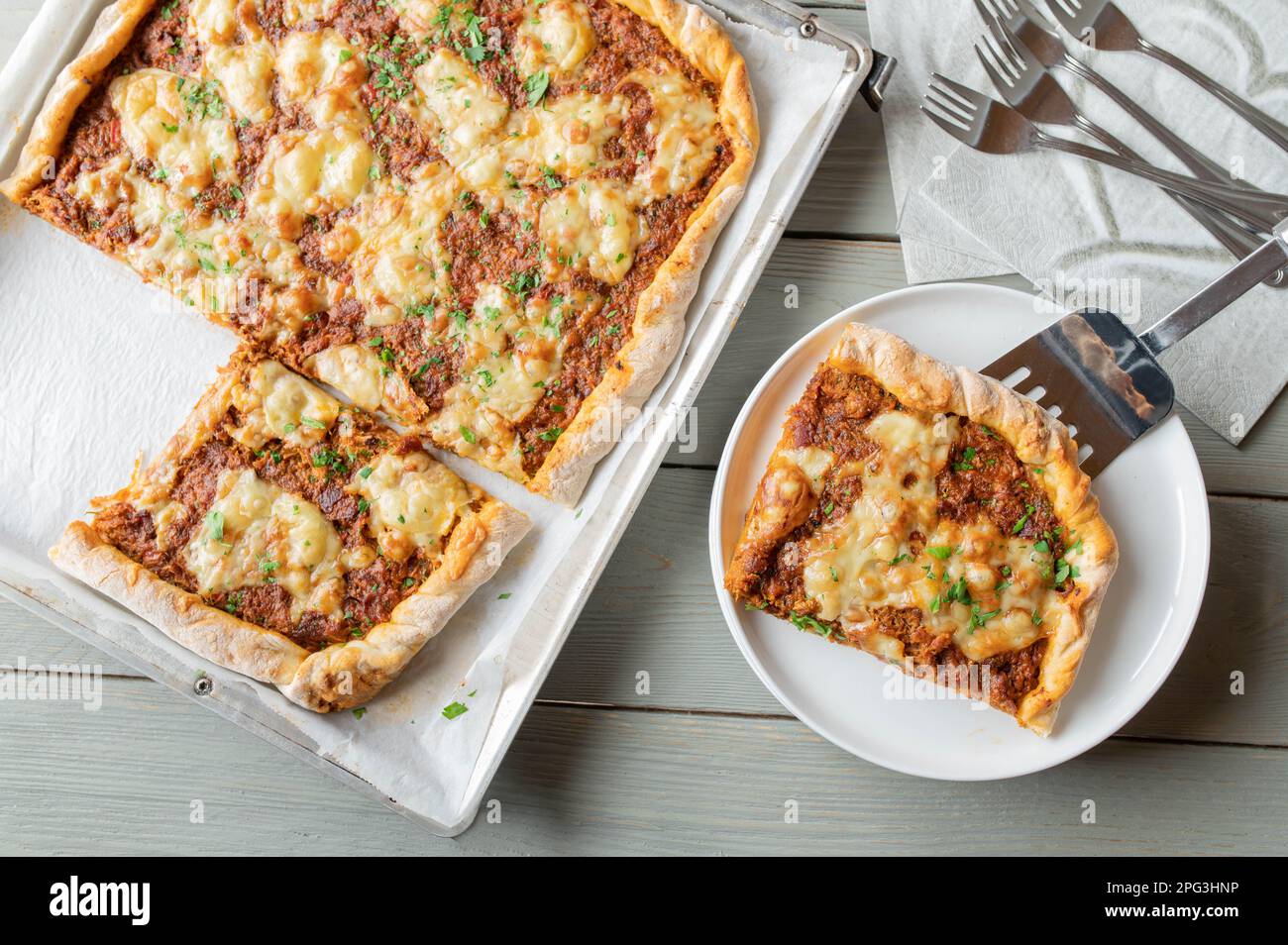 Pizza con carne di manzo macinata, formaggio, pomodori, cipolle, peperoni ed erbe aromatiche su un foglio da forno e un piatto Foto Stock