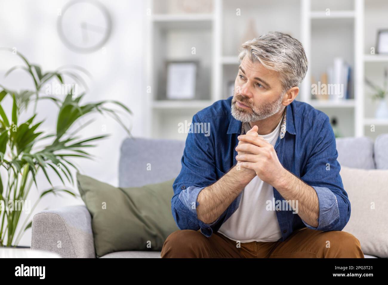 Adulto uomo maturo pensivo seduto da solo a casa sul divano primo piano, la persona con capelli grigi pensa guarda verso la finestra, depresso triste. Foto Stock