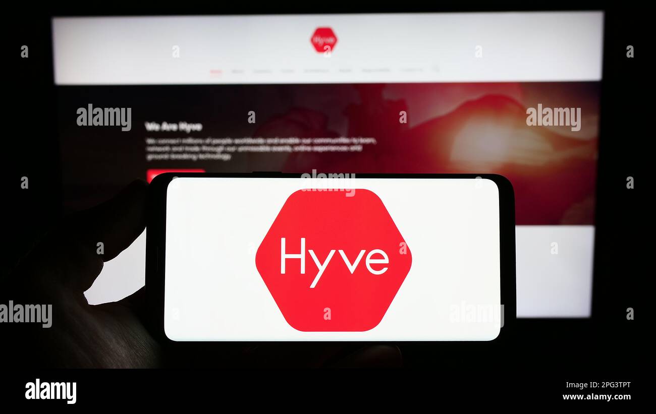 Persona che tiene uno smartphone con il logo della società britannica di gestione eventi Hyve Group plc sullo schermo di fronte al sito Web. Messa a fuoco sul display del telefono. Foto Stock