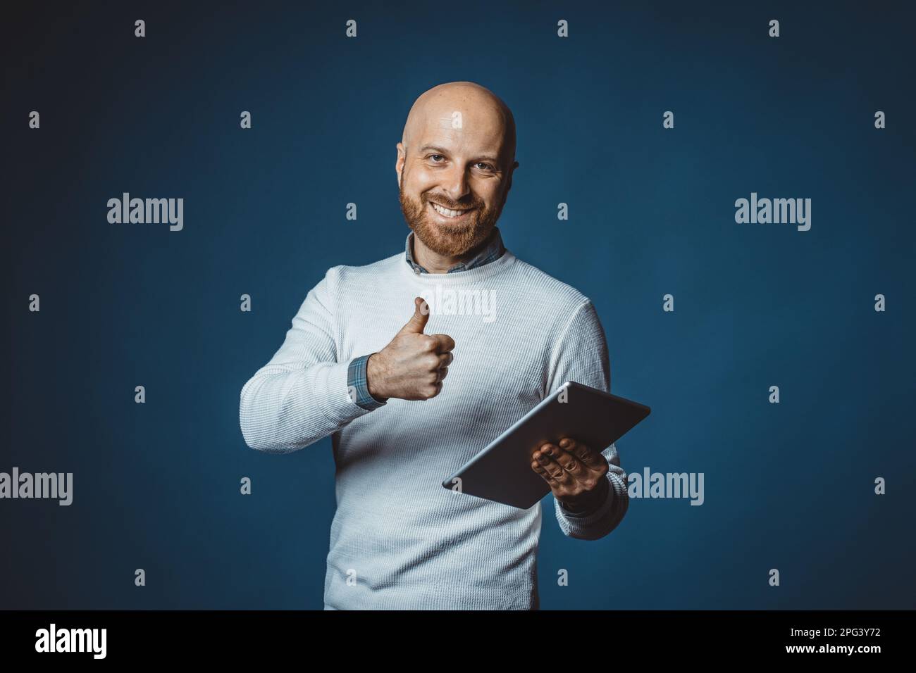 Ritratto fotografico di un simpatico ragazzo caucasico adulto con barba che naviga in rete tenendo una tavoletta con sfondo blu. Tecnico che utilizza un dispositivo portatile Foto Stock