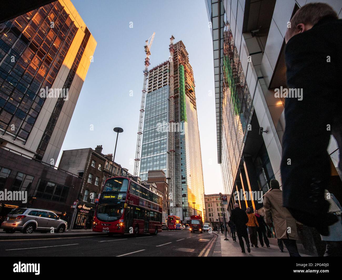 I pedoni e il traffico passano davanti al grattacielo degli uffici della Heron Tower in costruzione nel quartiere finanziario della City of London. Foto Stock