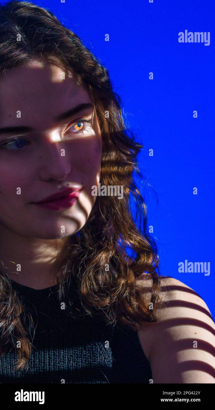 Primo piano di ragazza Teenage guardando fuori Camera con un occhio illuminato | maschera Gobo | Moda | Studio Lighting | sfondo blu reale Foto Stock