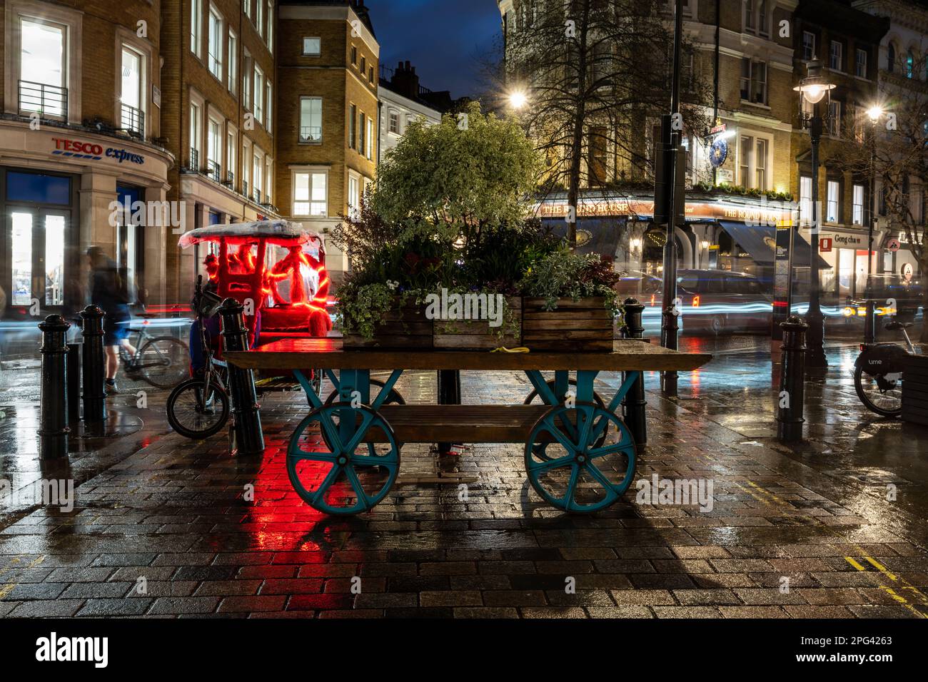 Un tradizionale carrello a mano decorato con scatole di piantatrice in legno blocca i veicoli a motore da King Street vicino a Covent Garden nel centro di Londra. Foto Stock