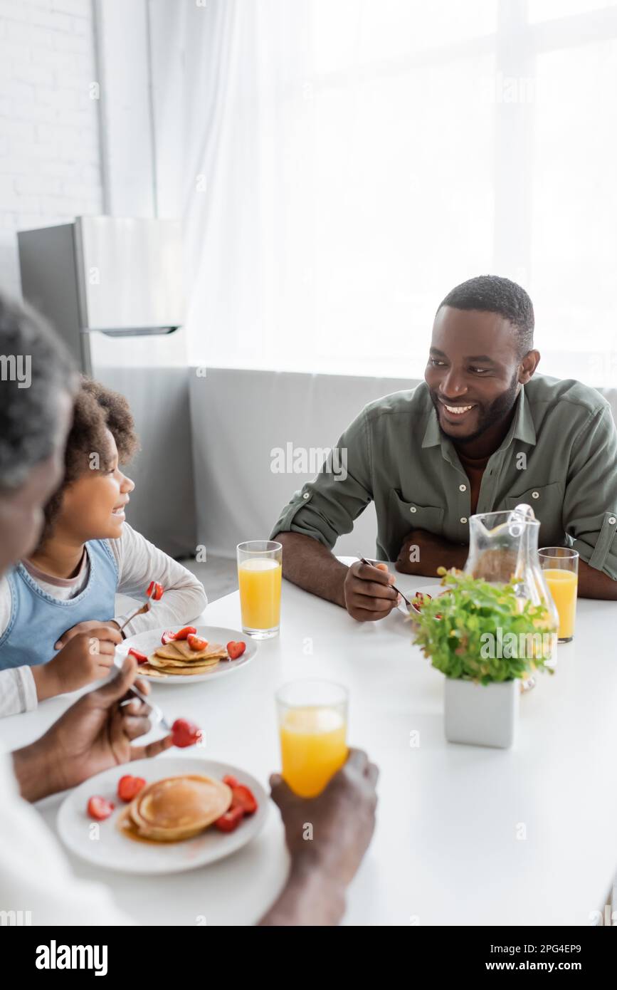 ragazza afro-americana felice guardando padre allegro mentre hanno la colazione della famiglia, immagine di scorta Foto Stock