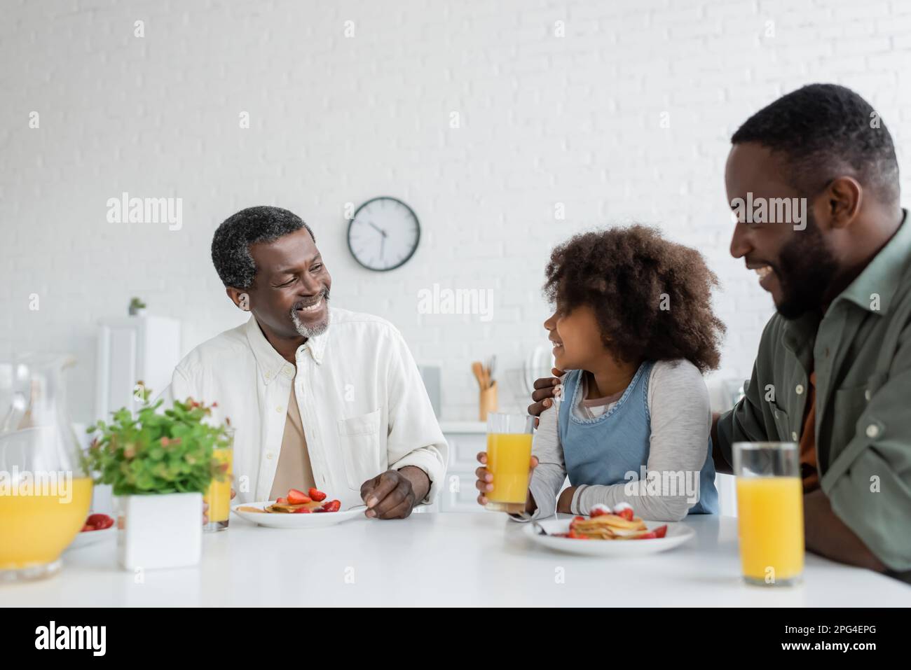 felice uomo di mezza età che guarda la nipote afroamericana vicino al figlio durante la colazione di famiglia, immagine stock Foto Stock