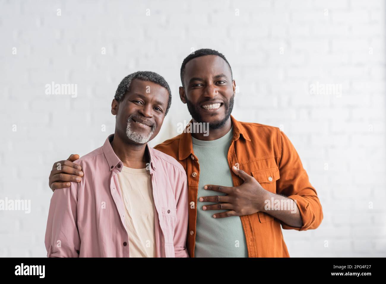 Uomo afro-americano spensierato abbracciando il genitore e guardando la fotocamera a casa, immagine di scorta Foto Stock