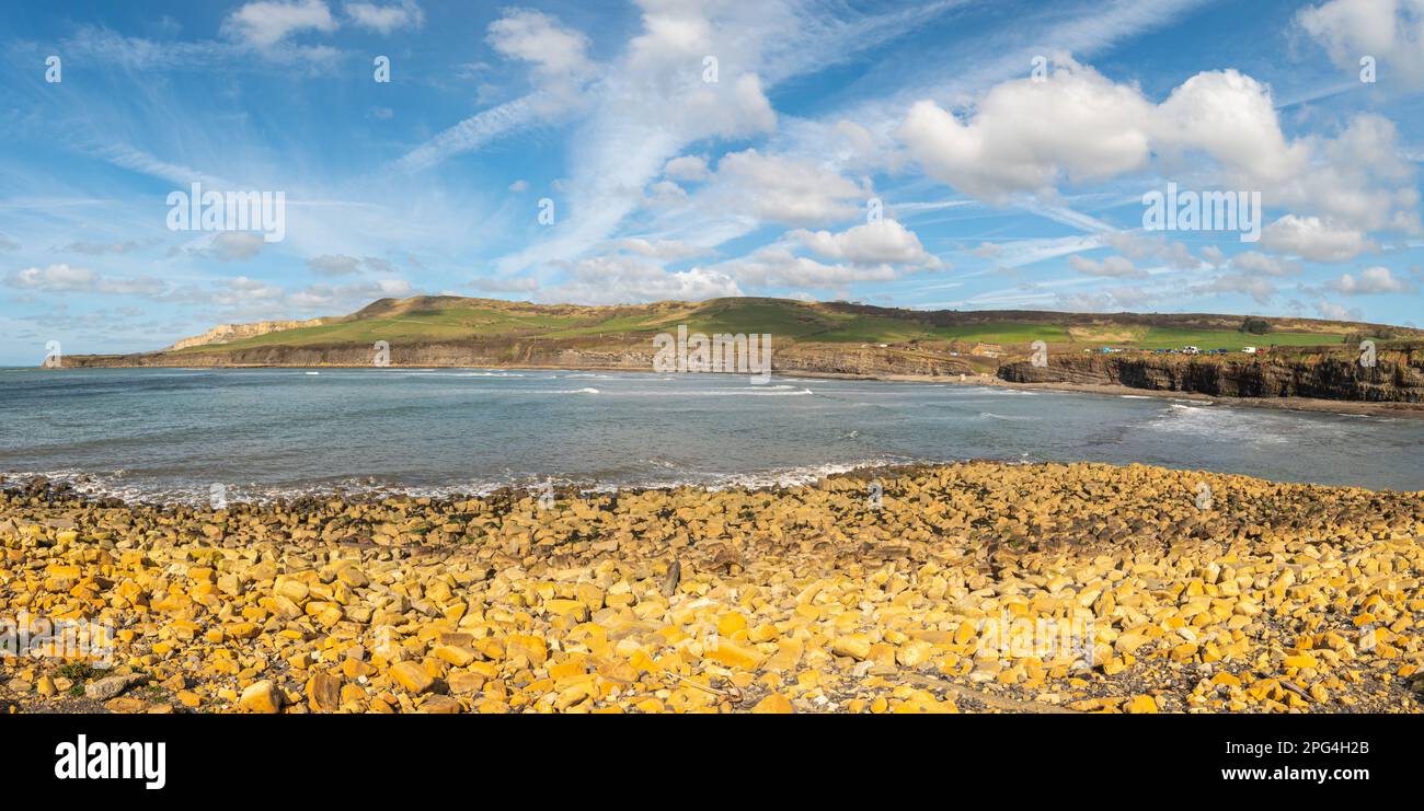 Rocce di argilla arancione in primo piano che si affaccia sulla baia di Kimmeridge e le scogliere Jurassic e parcheggio in una giornata di sole con nuvole leggere Foto Stock