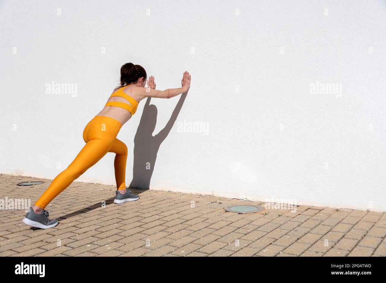 Adatta una donna sportiva che fa esercizi di stretching contro una parete. Foto Stock