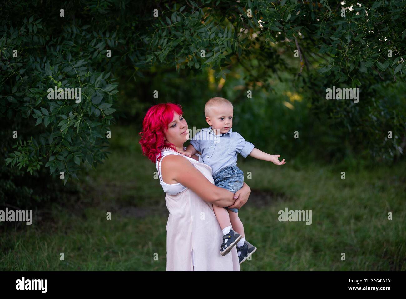 Ritratto di luce, diversità, straordinaria madre e figlio piccolo abbracciare nella foresta. Donna ha capelli rosa. Tenera maternità, felice infanzia. Ris Foto Stock
