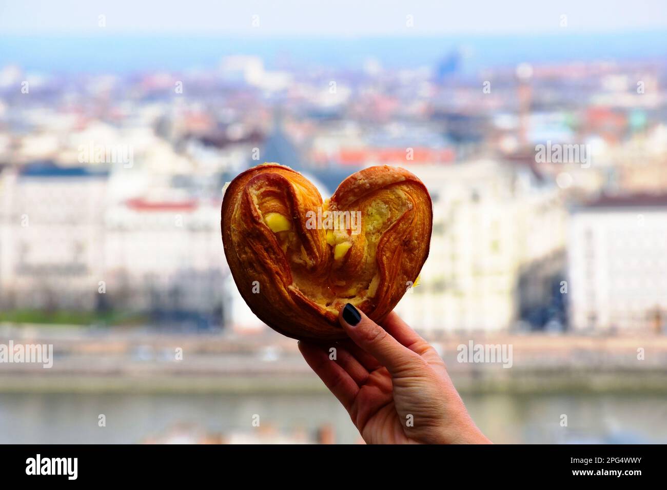 vista in primo piano della pasta decorativa a forma di cuore in mano femminile con sfondo morbido sfocato del paesaggio urbano. fette di mandorla bianche gialle. concetto di cibo Foto Stock