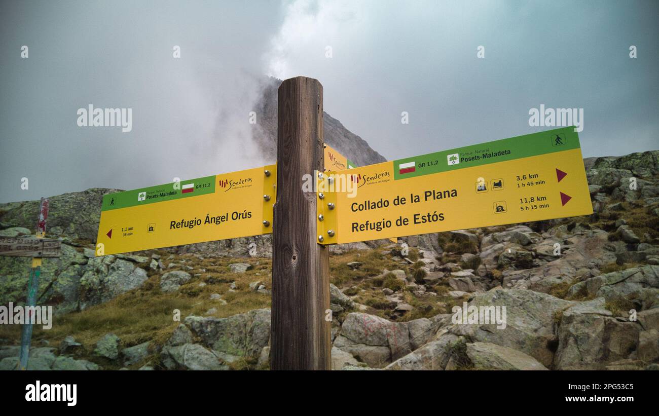 Due segnali gialli luminosi che indicano in direzioni diverse, che raffigurano un percorso per un sentiero escursionistico in una regione montuosa, Pontos, Spagna Foto Stock