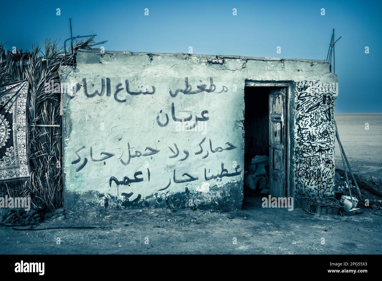 Questa suggestiva fotografia mostra un magazzino in decadenza nel deserto tunisino, con iscrizioni arabe sbiadite che adornano le sue pareti. L'edificio e' a s Foto Stock