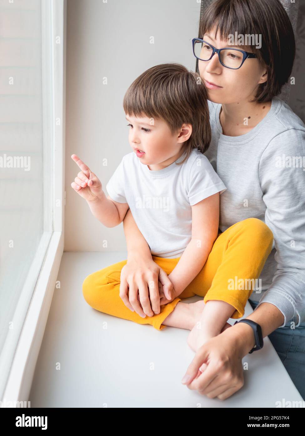 Donna triste guarda la finestra. Soggiorno forzato a casa a causa di coronavirus COVID-19 quarantena pandemia. Madre e figlio. Mamma e bambino. Foto Stock