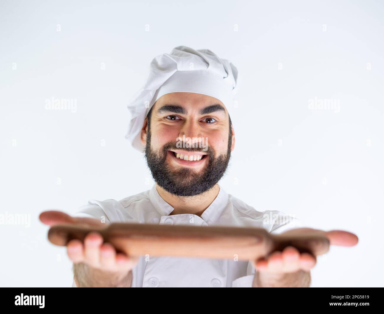Giovane cuoco maschio che mostra un perno di legno mentre sorride e guarda la macchina fotografica. Isolato su sfondo bianco Foto Stock
