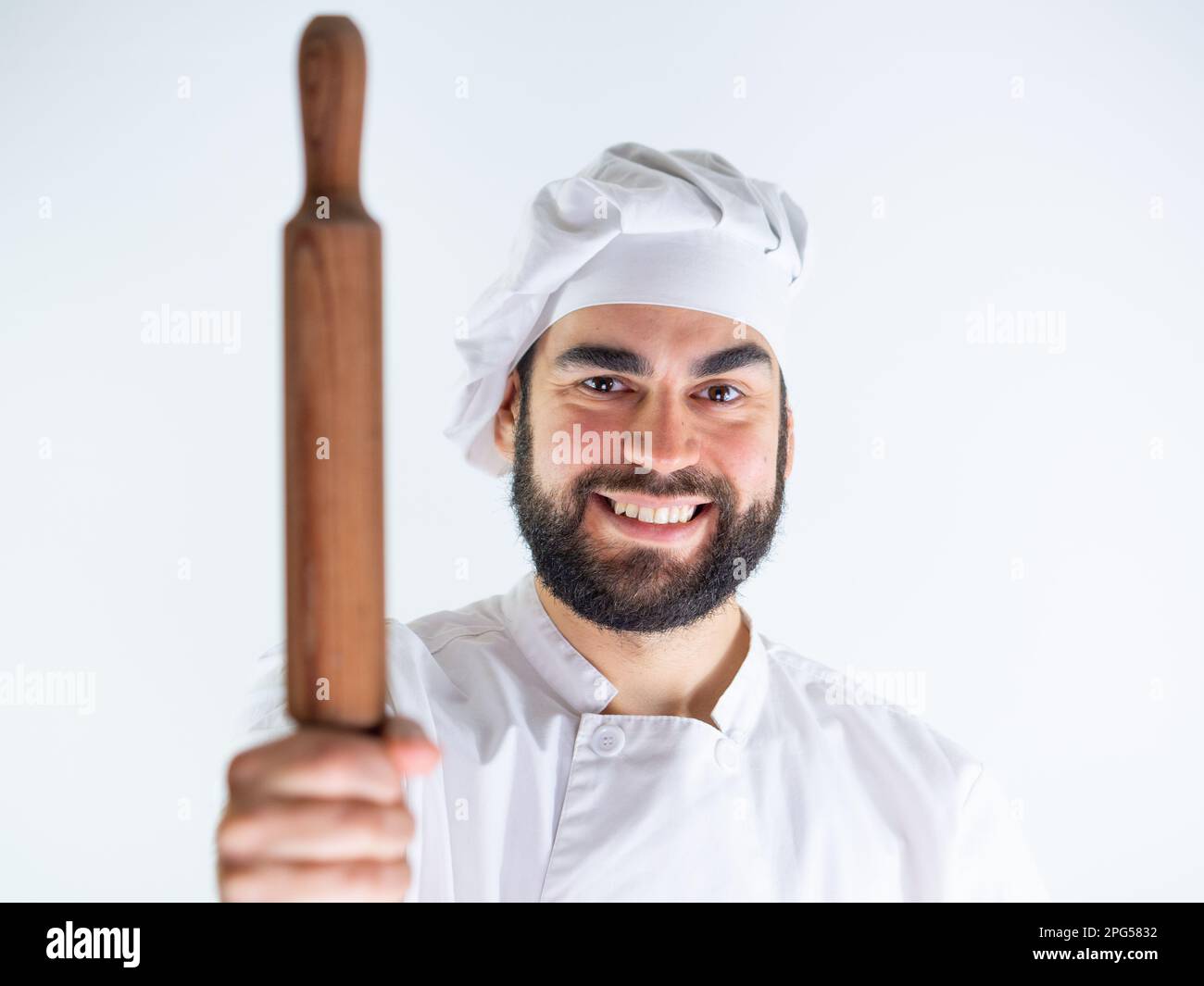 Giovane cuoco maschio che mostra un perno di legno mentre sorride e guarda la macchina fotografica. Isolato su sfondo bianco Foto Stock