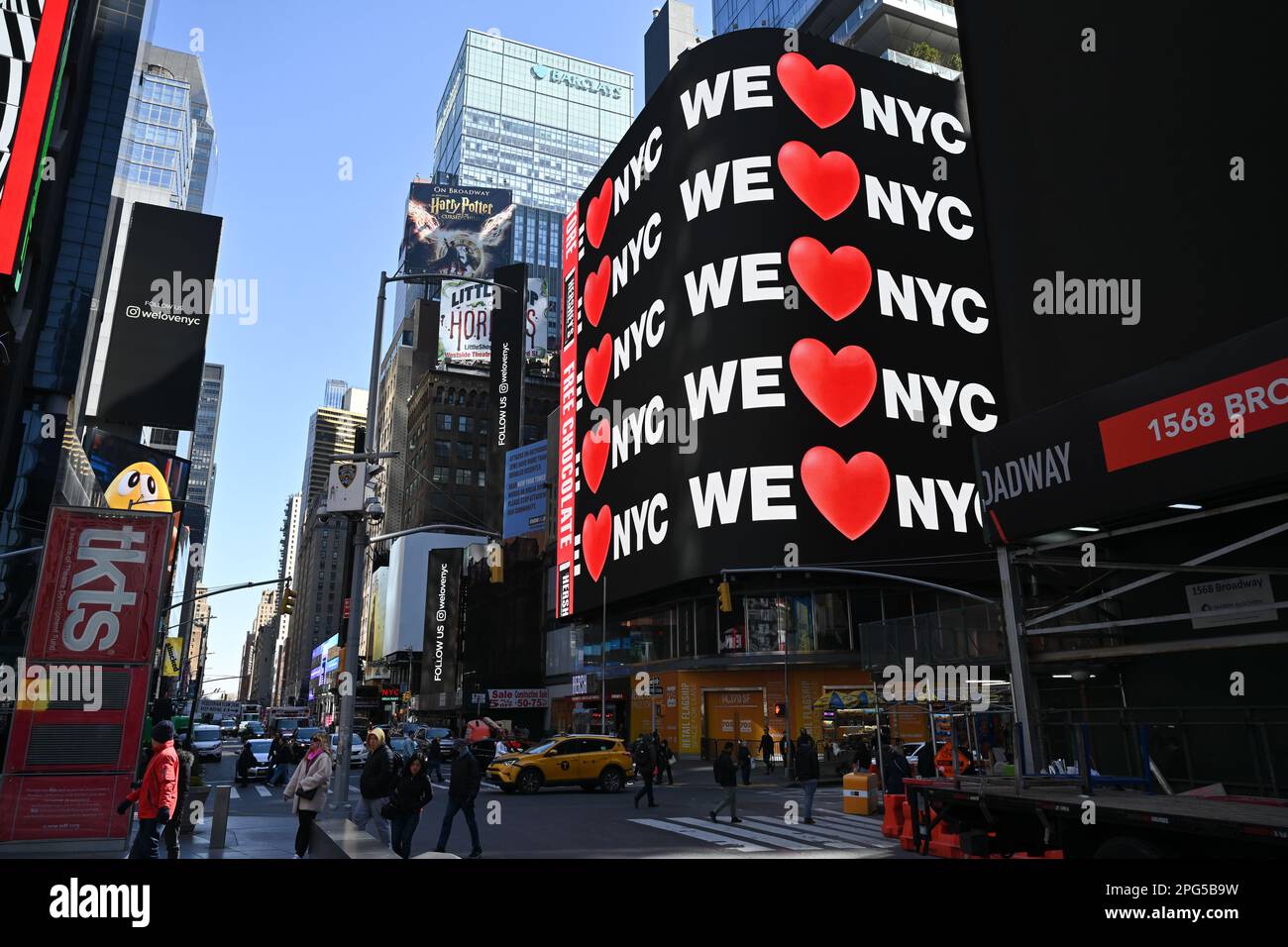 Le persone camminano vicino a cartelloni digitali che mostrano 'We Love NYC' durante l'evento di lancio della campagna per 'We Love NYC' a Times Square il 20 marzo 2023 in N Foto Stock