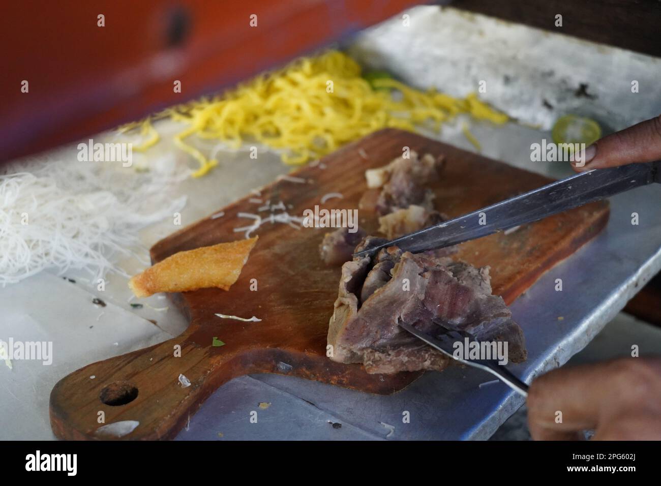 Il brisket di manzo viene tagliato a pezzetti su un tagliere di legno. con spaghetti gialli sullo sfondo. Preparazione per la zuppa di noodle di manzo in Indonesia. Foto Stock