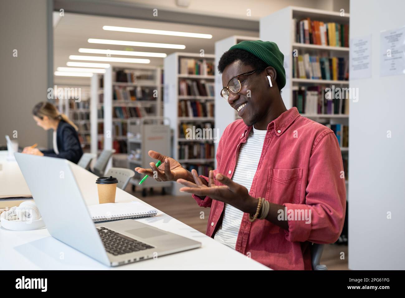 Sorridente studente nero o freelancer in cuffie utilizzando un computer portatile guardando lo schermo facendo videochiamata. Foto Stock