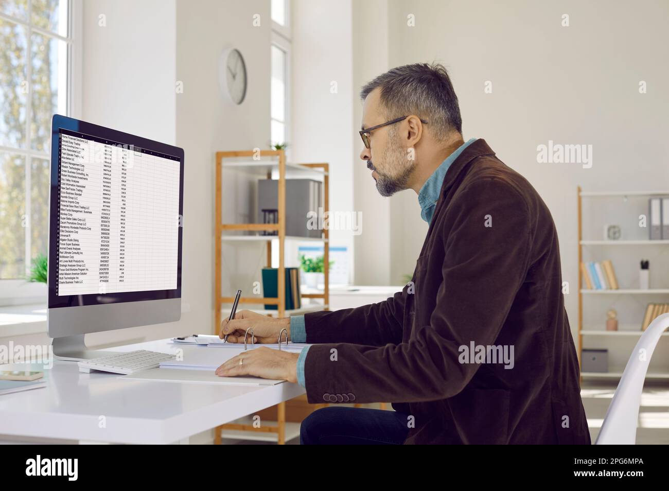 Ritratto di uomo d'affari serio, attento, maturo con gli occhiali, seduto sul posto di lavoro e guardando lo schermo del suo computer. Foto Stock
