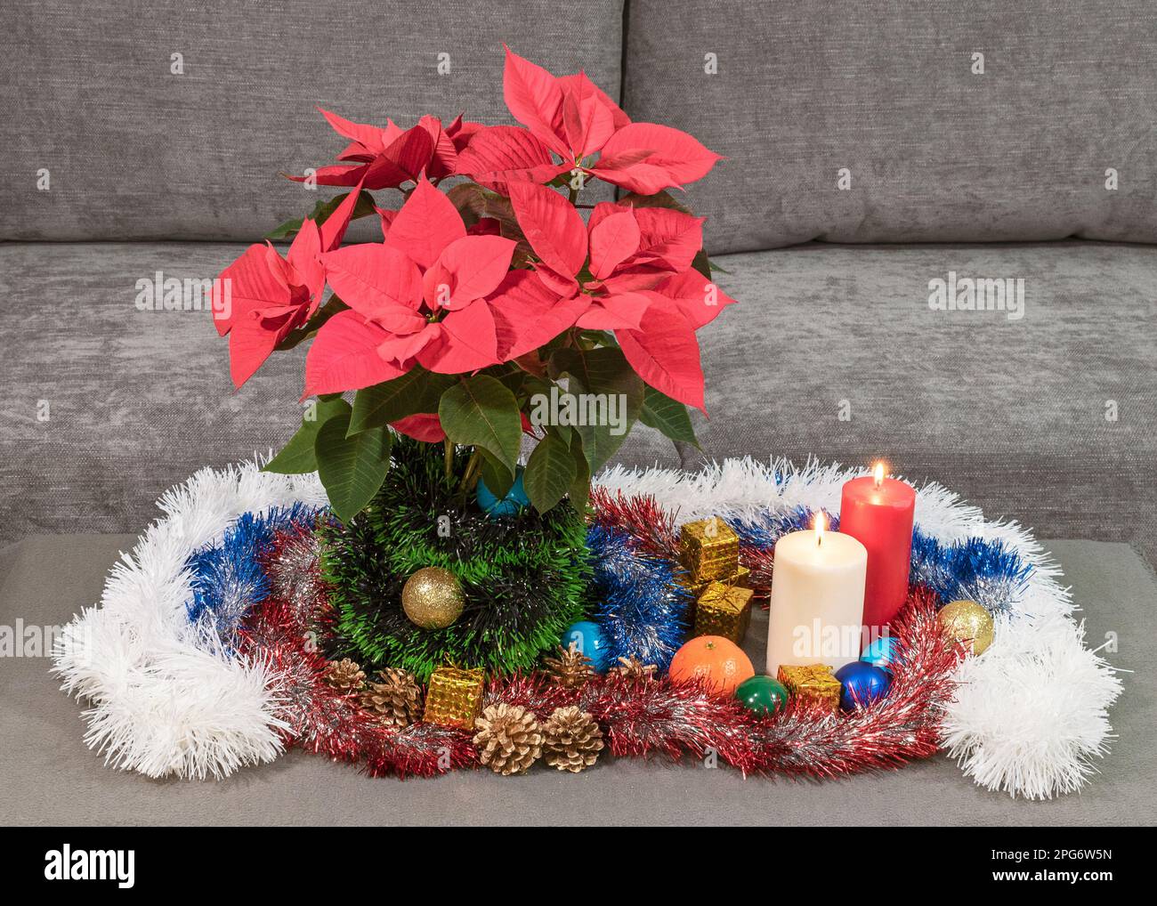 Inverno Natale decorazione tavolo vacanza con una poinsettia rosso brillante e ornamenti tradizionali con tinsel e due candele brucianti Foto Stock