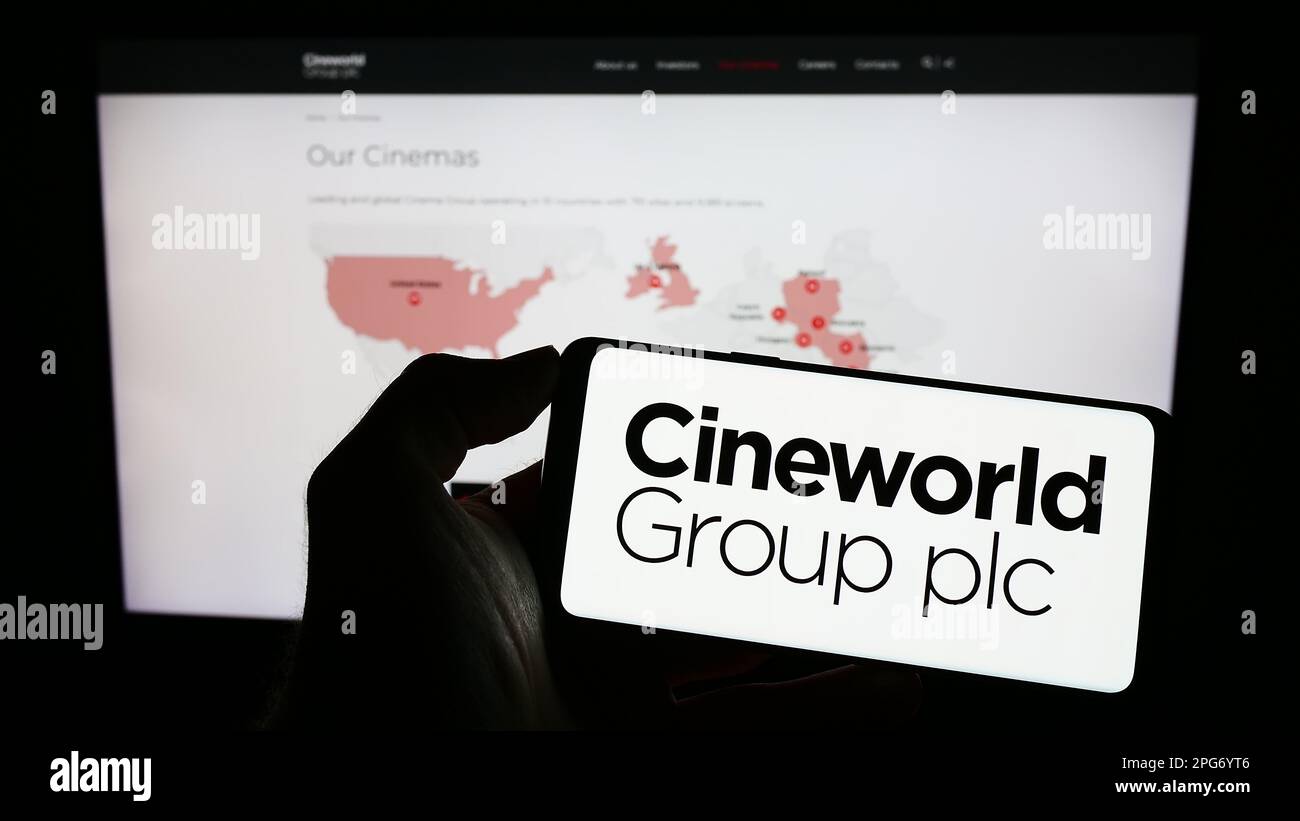 Persona che tiene uno smartphone con il logo della società cinematografica britannica Cineworld Group plc sullo schermo di fronte al sito Web. Messa a fuoco sul display del telefono. Foto Stock