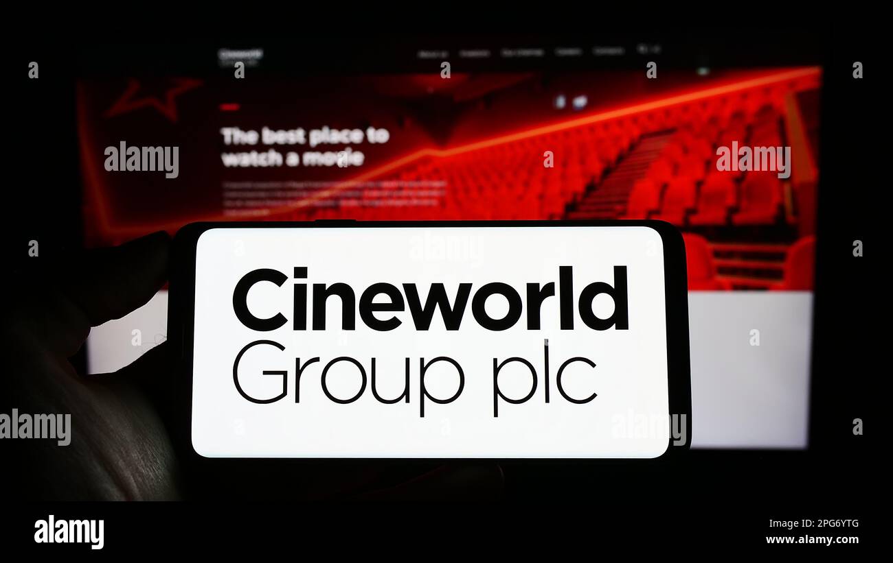 Persona che tiene il cellulare con il logo della società cinematografica britannica Cineworld Group plc sullo schermo di fronte al sito web aziendale. Messa a fuoco sul display del telefono. Foto Stock