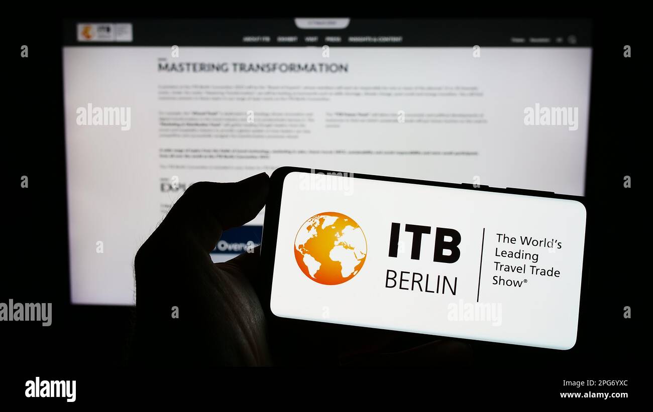 Persona che tiene il cellulare con il logo della fiera turistica tedesca ITB Berlin sullo schermo di fronte alla pagina web. Messa a fuoco sul display del telefono. Foto Stock