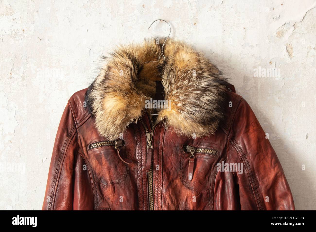 giacca invernale da donna in pelle di pelliccia rossa appesa a un appendiabiti su una parete bianca all'interno Foto Stock